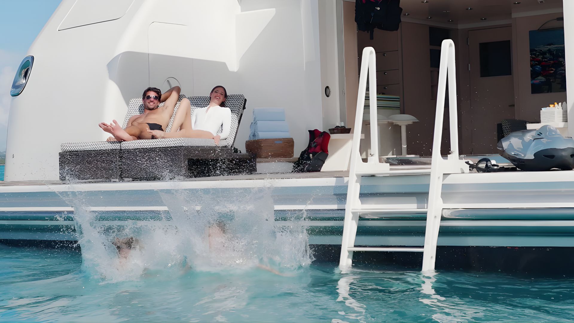 Couple se relaxant sur le pont arrière d’un yacht de luxe tandis qu’un plongeon éclabousse la mer turquoise, scène de croisière privée et location de yacht à Saint-Tropez avec Azur Dream.