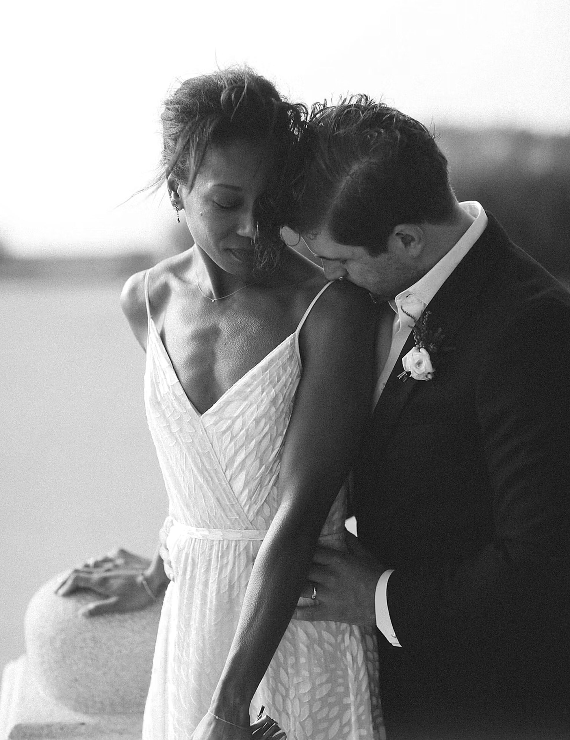The groom kisses the bride on the shoulder facing the sea, black and white portrait, wedding in Saint-Tropez