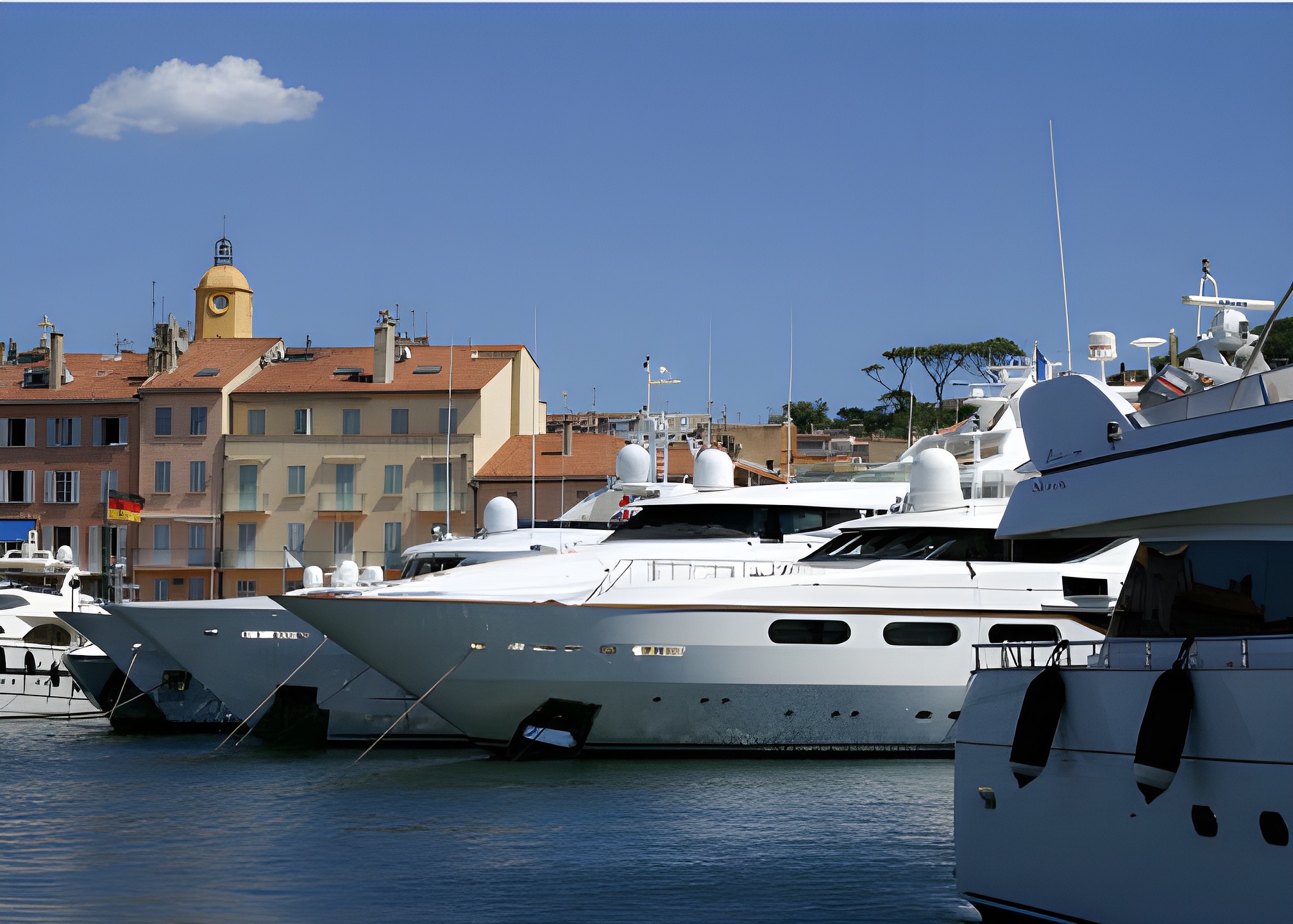 Luxury yachts moored in Saint-Tropez harbour in front of the quayside façades and the bell tower
